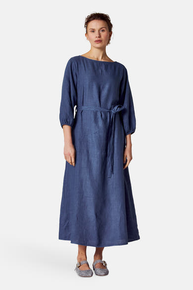 Blauwe jurk van COPINES D'ANVERS met een strikceintuur, gedragen met gestreepte schoenen.