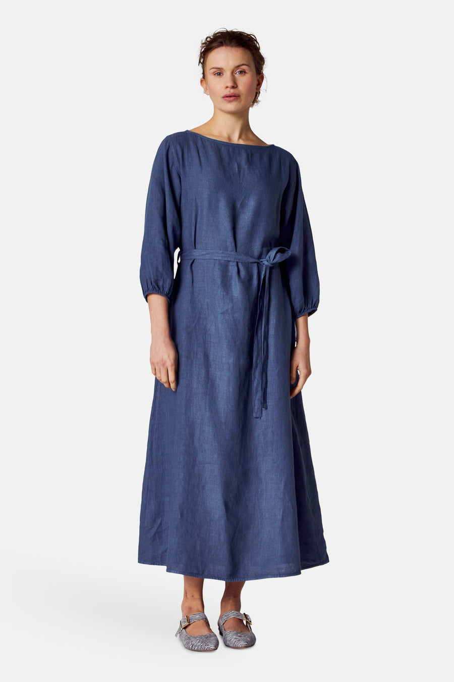 Blauwe jurk van COPINES D'ANVERS met een strikceintuur, gedragen met gestreepte schoenen.