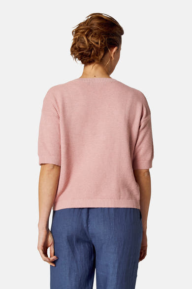 Ronde hals roze trui van COPINES D'ANVERS, in ribgebreid, gedragen met een blauwe broek.