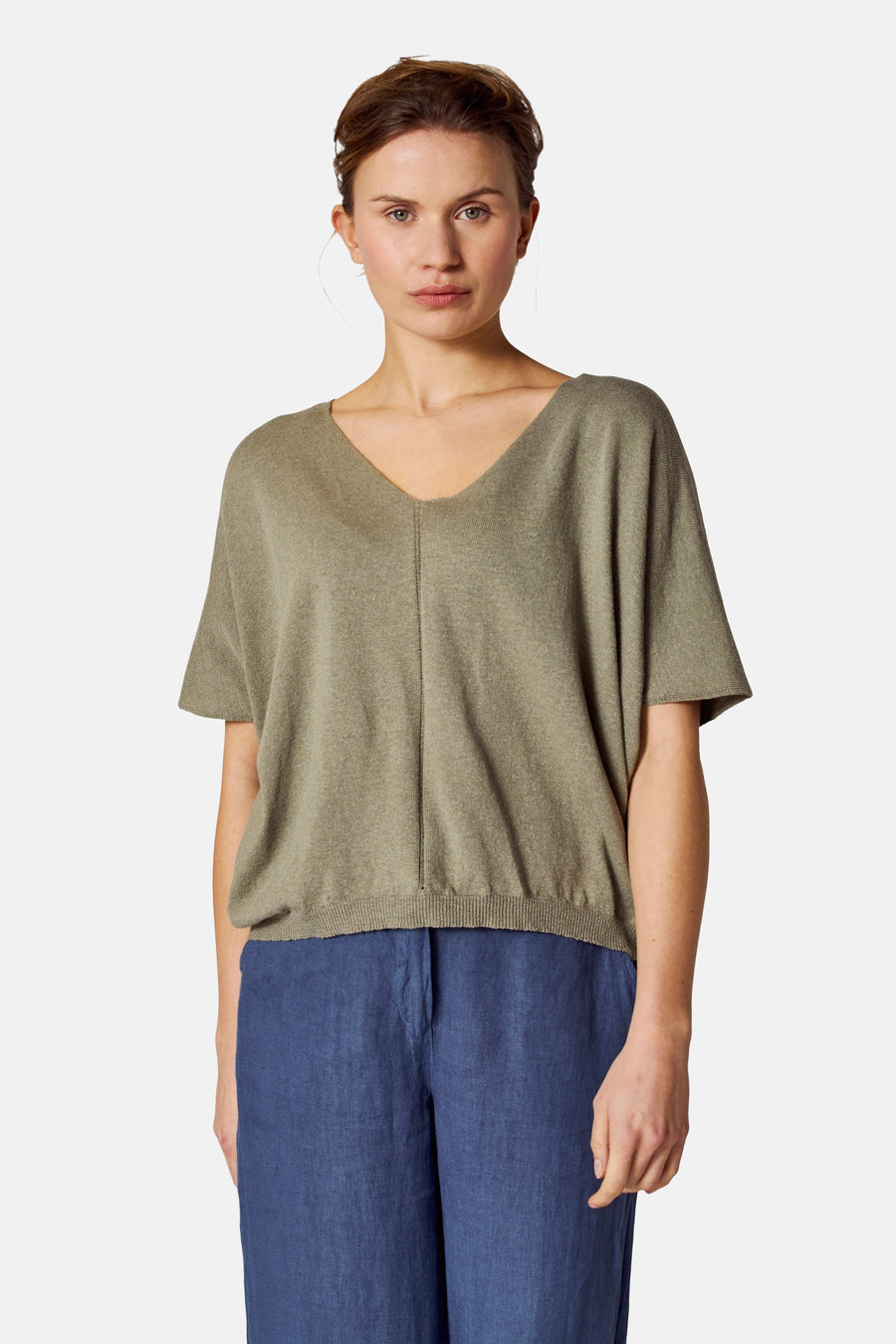 Top vert en tricot de COPINES D'ANVERS, avec un col en V et des manches courtes, porté avec un pantalon bleu.
