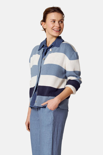 Blauwe jas van COPINES D'ANVERS met witte en donkere blauwe strepen, gedragen met een blauwe shirt en broek.