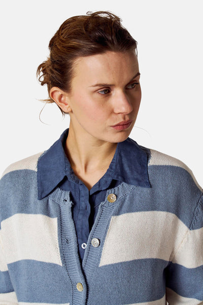 Gilet bleu en maille rayée de Copines D'Anvers, porté sur une chemise bleu marine boutonnée.