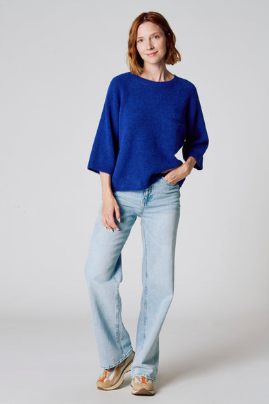 Ronde hals trui blauw van COPINES D'ANVERS, gedragen met een wijde lichtblauwe jeans en meerkleurige sneakers.
