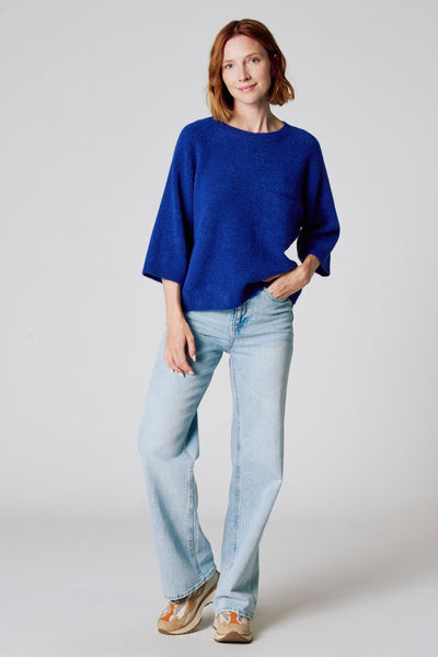Ronde hals trui blauw van COPINES D'ANVERS, gedragen met een wijde lichtblauwe jeans en meerkleurige sneakers.
