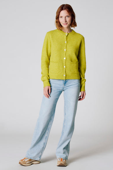 Groene cardigan van Copines d'Anvers, met witte knopen, gedragen met een lichte jeans en sneakers.