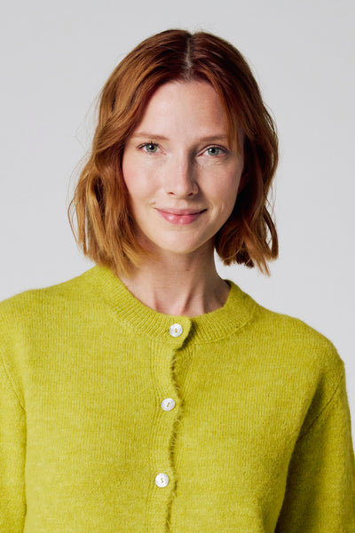 Mosterdgroene cardigan van Copines d'Anvers, met een gebreide textuur en witte knopen.