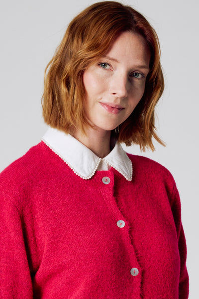 Roze cardigan met parelmoer Peter Pan-kraag van Copines d'Anvers, gedragen met een blouse met witte kraag.