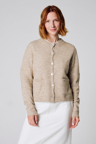 Taupe vest van Copines D'Anvers, met zakken en parelmoeren knopen, gedragen met een witte rok.