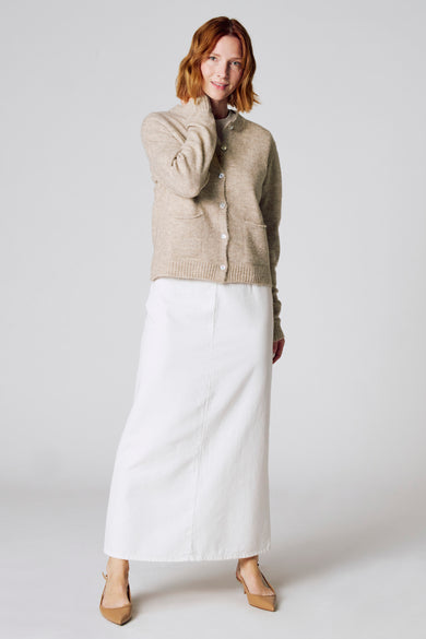 Taupe gebreid vest van COPINES D'ANVERS, gedragen met een lange witte rok en bruine pumps.