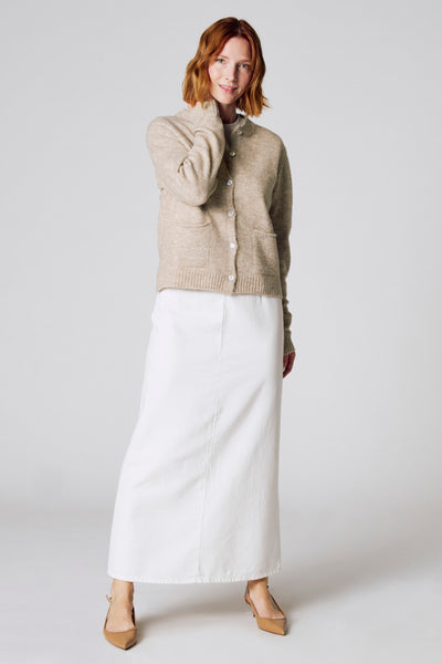 Taupe gebreid vest van COPINES D'ANVERS, gedragen met een lange witte rok en bruine pumps.