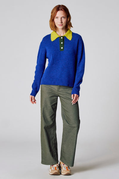 Pull col rond bleu de COPINES D'ANVERS avec col vert anis, porté avec un pantalon vert olive et des baskets multicolores.