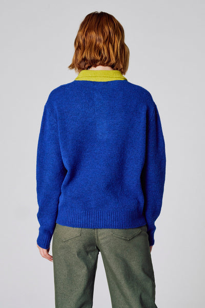 Pull à col rond bleu de COPINES D'ANVERS, avec col vert anis, porté avec un pantalon vert olive, vue de dos.
