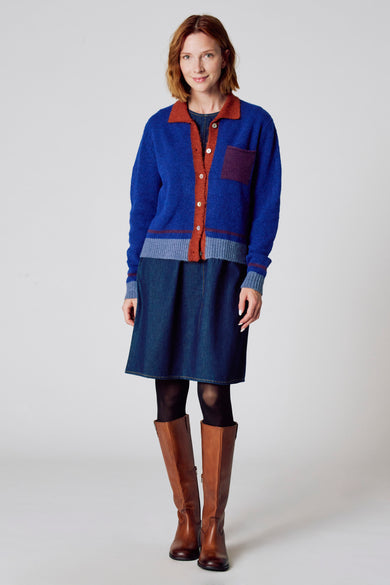 Blauwe cardigan met ronde hals van COPINES D'ANVERS, gedragen met een spijkerjurk, zwarte panty en bruine laarzen.