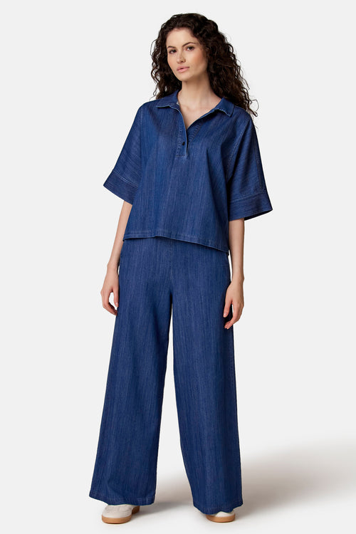 Blauwe spijkerblouse van COPINES D'ANVERS met polokraag, korte mouwen en een relaxte pasvorm, gedragen met een bijpassende wijde broek.