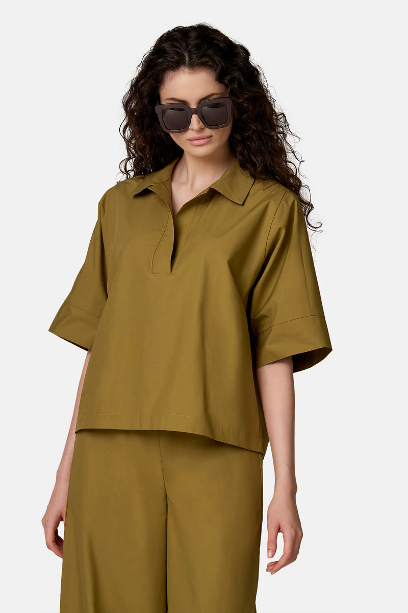 Kaki groen blouse van COPINES D'ANVERS met korte mouwen en een losse pasvorm, van opzij gedragen met een bijpassende broek en een zonnebril.