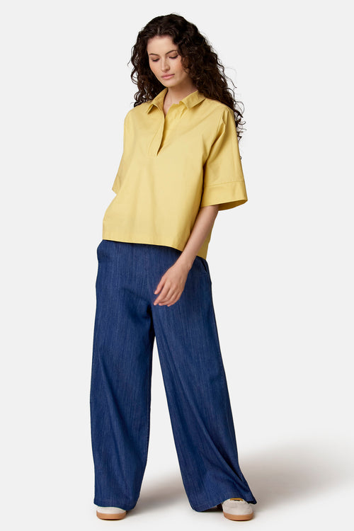 Gele, losvallende blouse met korte mouwen van COPINES D'ANVERS, polostijl met V-hals, gedragen met een wijde blauwe spijkerbroek.