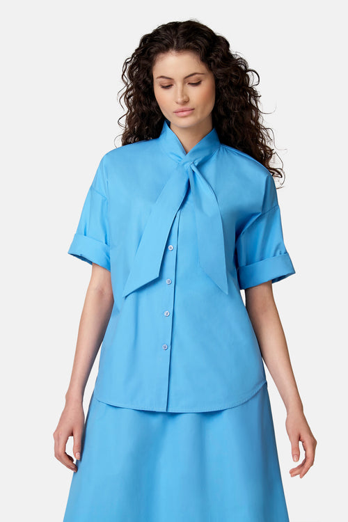Blauwe blouse met korte opgerolde mouwen, opstaande kraag en losse pasvorm van COPINES D'ANVERS, van achteren gezien.