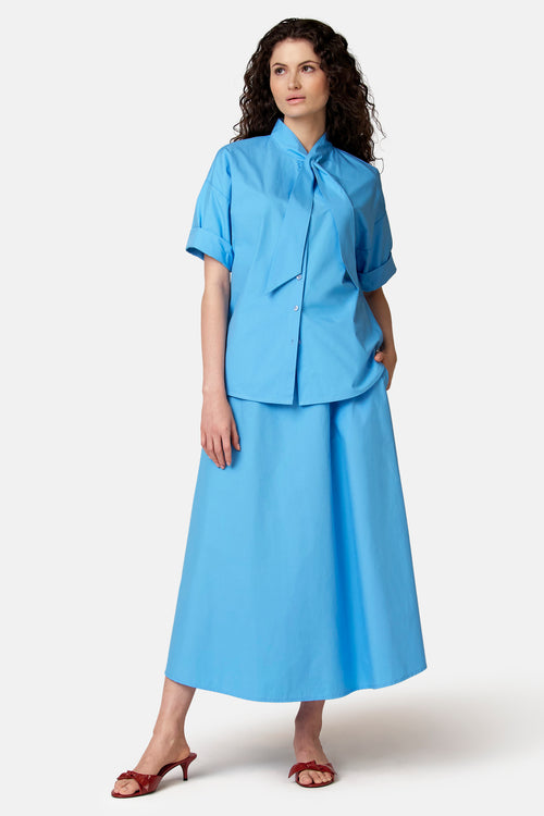 Blauwe blouse van COPINES D'ANVERS met lavallièrekraag en korte opgerolde mouwen, gedragen met een bijpassende lange rok.