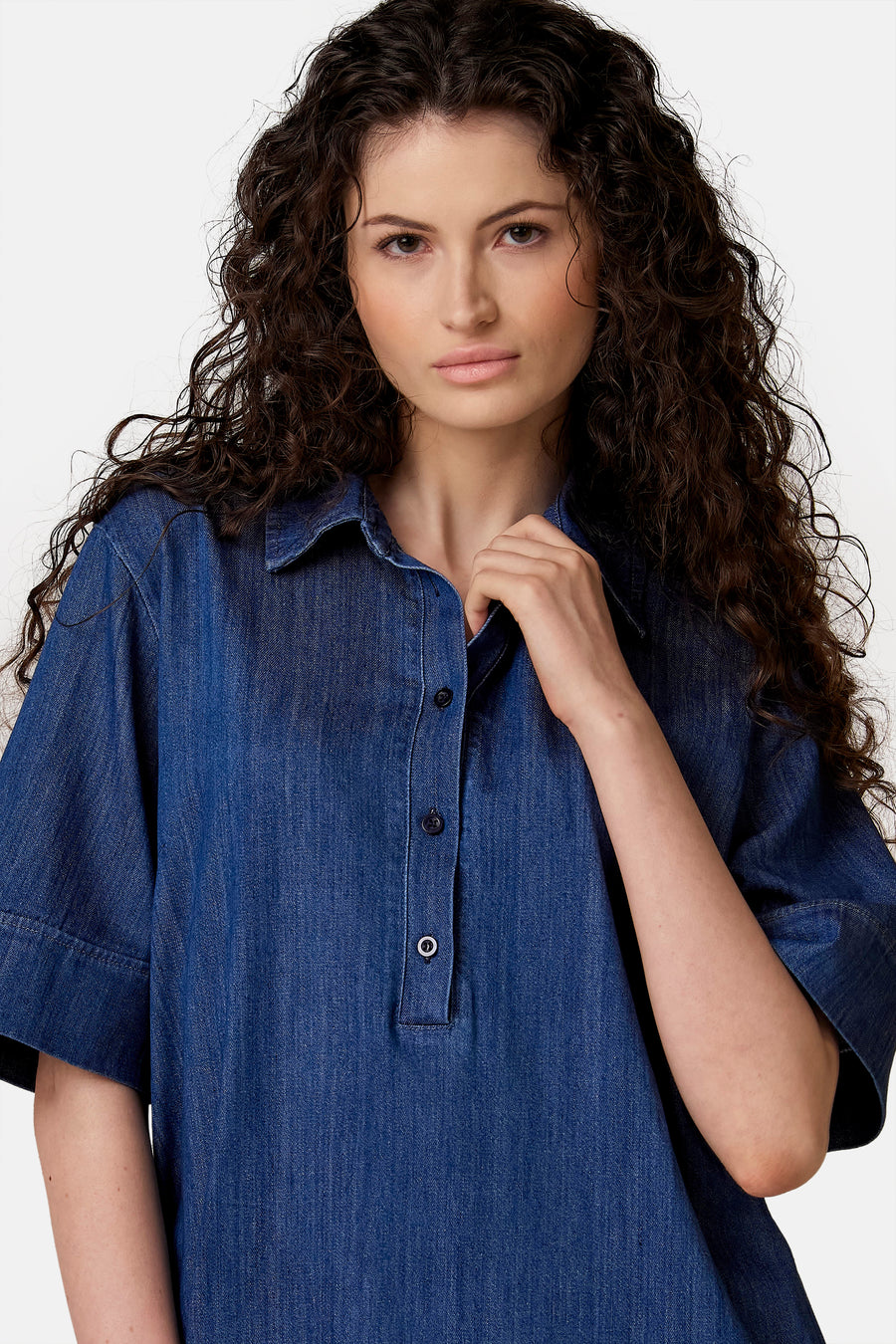 Robe chemise en jean bleu clair de COPINES D'ANVERS, à manches courtes, portée par une femme aux cheveux bouclés.