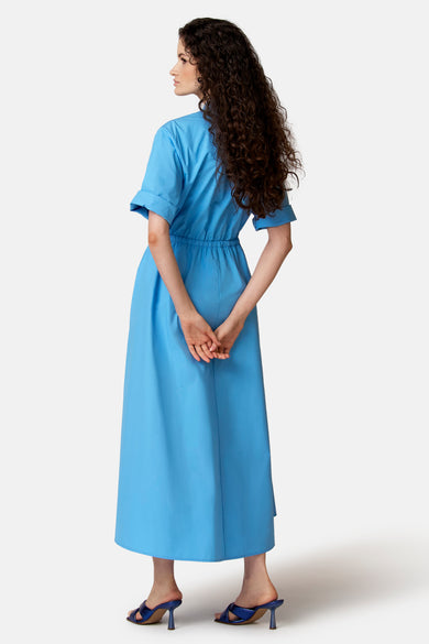 Lange blauwe jurk van COPINES D'ANVERS, met opgerolde korte mouwen en elastische taille, van achteren gezien.