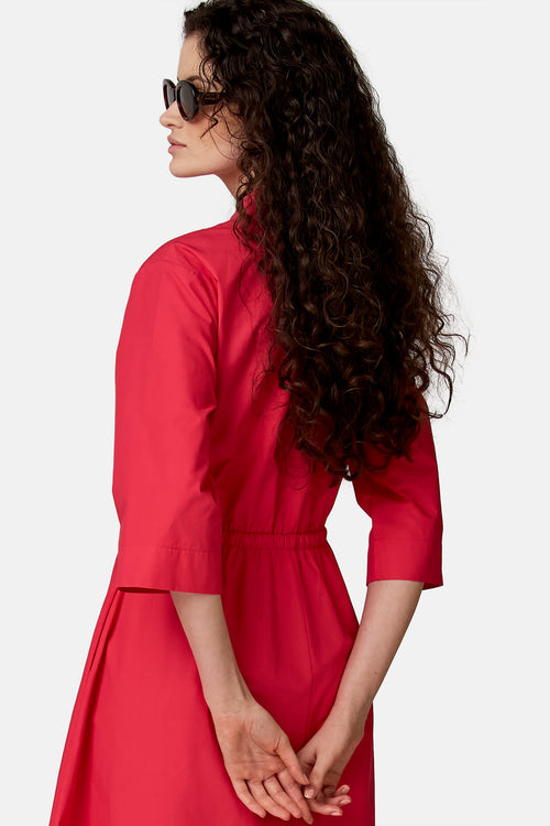 Roze overhemdjurk van COPINES D'ANVERS met 3/4 mouwen, elastische taille, van opzij gedragen door een vrouw met krullend haar en een zonnebril.