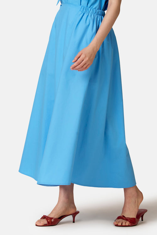 Jupe évasée bleue de COPINES D'ANVERS à taille élastiquée, longueur maxi, portée avec des mules rouges.