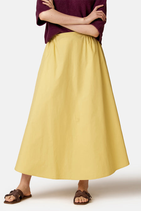 Jupe jaune de COPINES D'ANVERS, longue et évasée avec taille élastiquée, portée avec un pull bordeaux et des sandales marron.