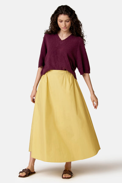 Jupe longue jaune de COPINES D'ANVERS, portée avec un pull bordeaux et des sandales marron.
