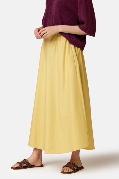 Jupe longue jaune de COPINES D'ANVERS, ample et fluide, taille élastiquée, portée avec un pull prune et des sandales marron.