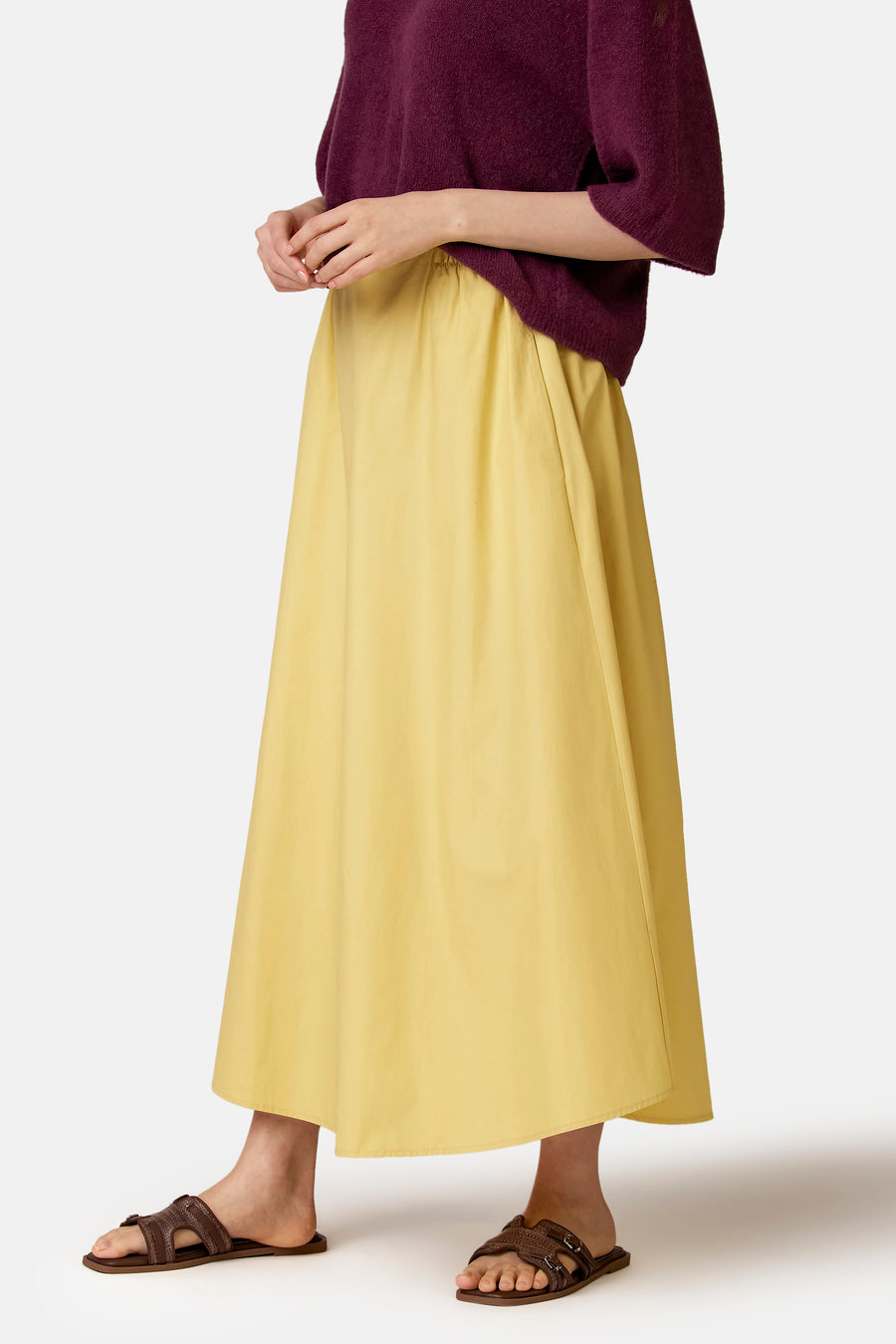 Jupe longue jaune de COPINES D'ANVERS, ample et fluide, taille élastiquée, portée avec un pull prune et des sandales marron.
