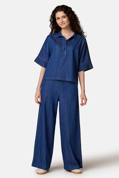 Pantalon large en denim bleu clair de COPINES D'ANVERS, porté avec un chemisier assorti et des baskets claires.