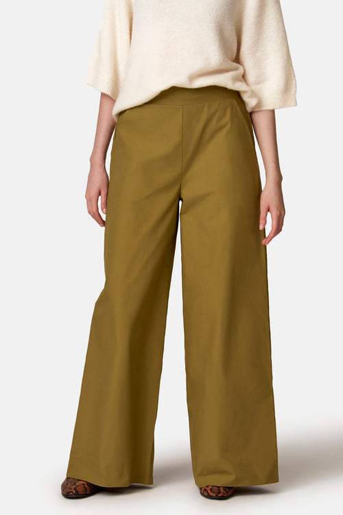 Olijfgroene wijde broek van COPINES D'ANVERS, met zijzakken, gedragen met een crèmekleurige trui en slangenleren loafers.