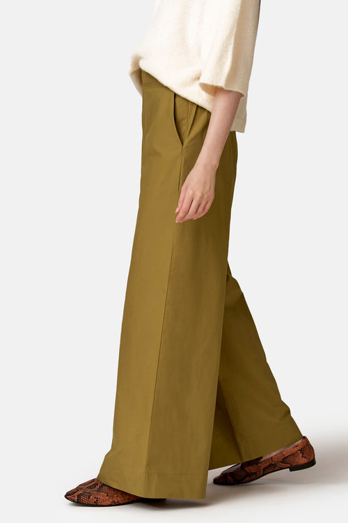 Pantalon ample vert olive de COPINES D'ANVERS, avec poches latérales, porté avec un pull crème et des mocassins serpent.
