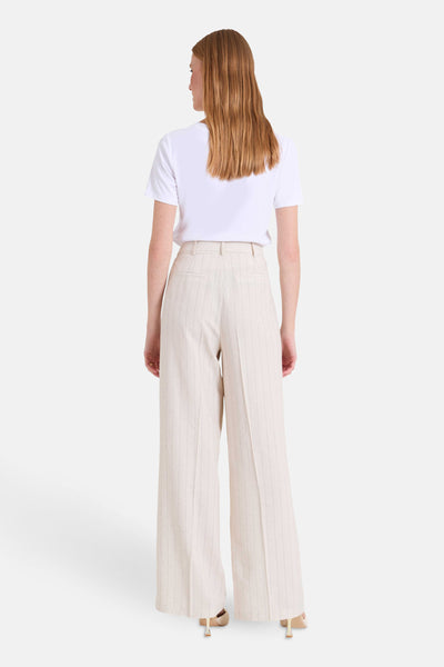 Pantalon beige rayé de NAF NAF, coupe ample, porté avec un t-shirt blanc et des talons clairs.