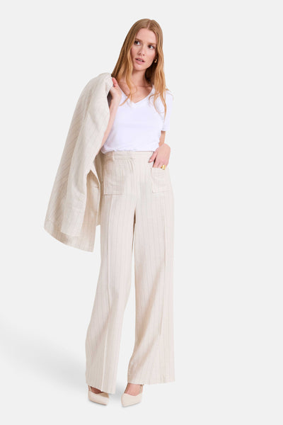 Pantalon beige rayé by NAF NAF, avec des poches et porté avec un t-shirt blanc et des talons clairs.