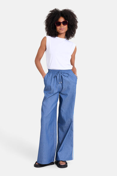 Wit mouwloos topje van NAF NAF, gedragen met een wijde blauwe broek en zwarte sandalen.