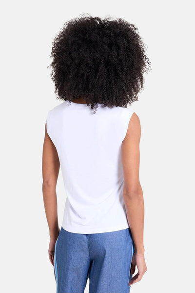 Wit mouwloos topje van NAF NAF, gedragen met een blauwe broek met zijstrepen.