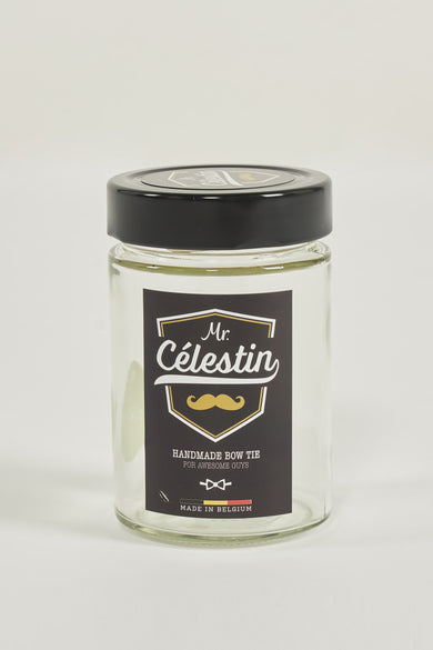 Nœud papillon orange dans un bocal en verre de Mr. Celestin, avec étiquette décorative et bouchon noir.
