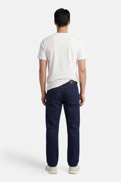 Ecru T-shirt van STROM, van achteren gedragen door een man met een donkerblauwe jeans en lichte sneakers.