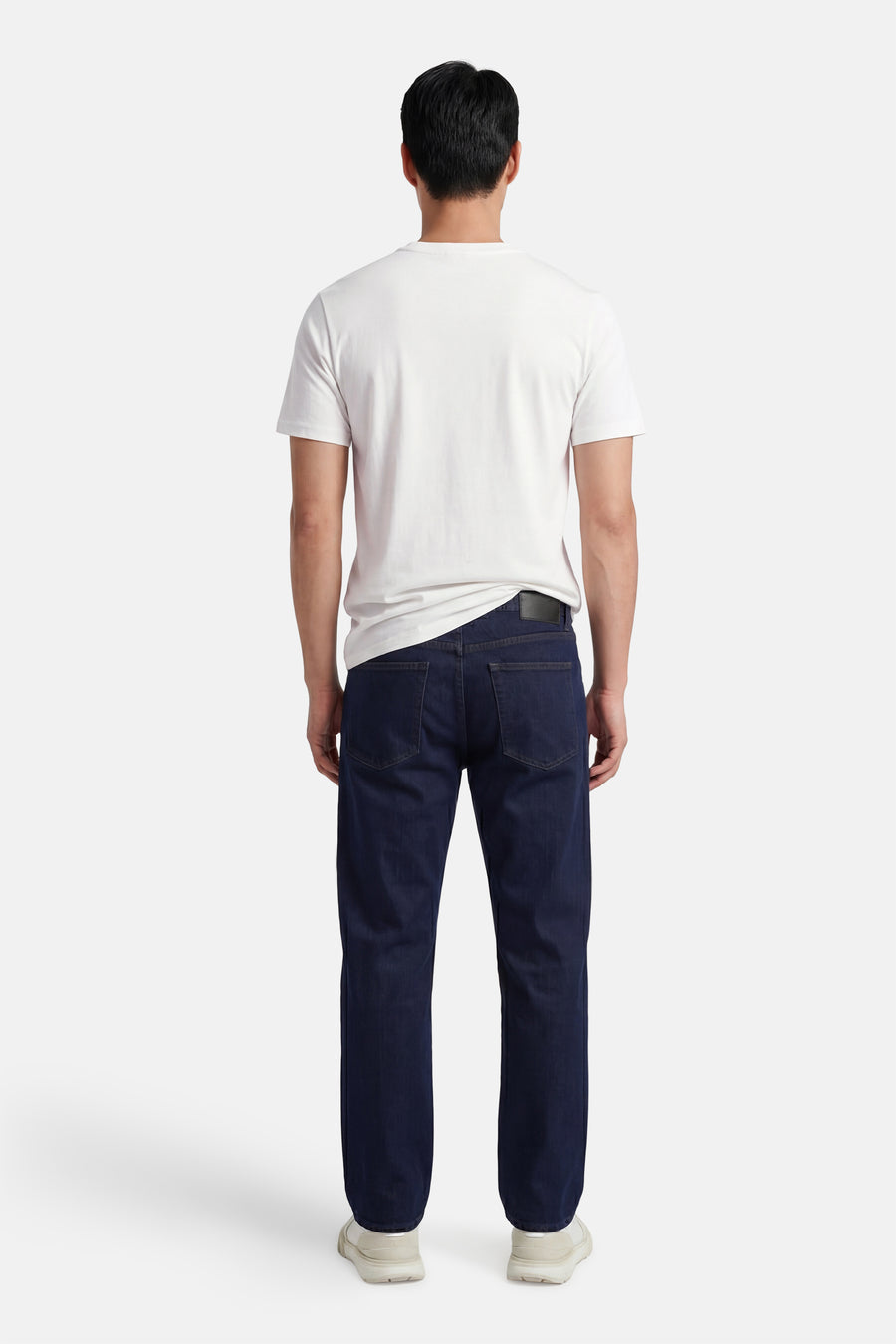 Ecru T-shirt van STROM, van achteren gedragen door een man met een donkerblauwe jeans en lichte sneakers.