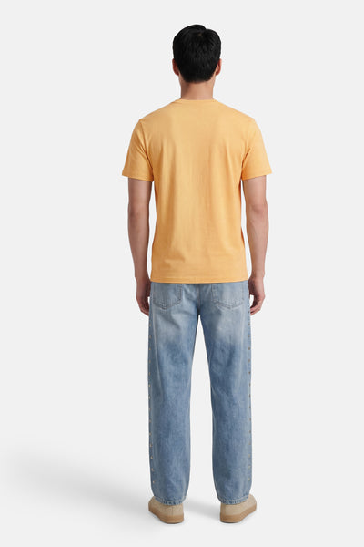 T-shirt jaune à manches courtes de STROM, vu de dos avec un jean clair à clous et des baskets beiges.