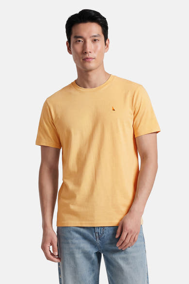 Gele STROM T-shirt met een klein zeilbootlogo op de borst, gedragen door een man in een verbleekte spijkerbroek.