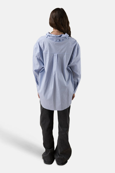 Chemise à manches longues bleue par ADORE, avec un collier doré, portée avec un pantalon noir.