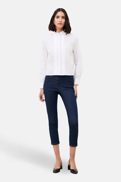 Chemise à manches longues blanche de CAROLL, avec détails plissés sur le devant, portée avec un jean et des escarpins noirs.
