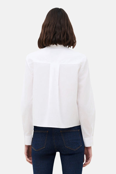 Chemisier à manches longues blanc de CAROLL, coupe courte avec pli creux au dos, porté avec un jean bleu foncé.
