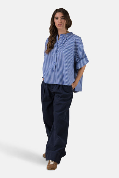 Blauwe blouse met lange mouwen en witte strepen van ADORE, gedragen met een marineblauwe broek en bruine schoenen.