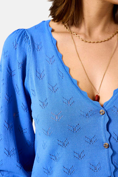 Cardigan bleu ajouré de GARCIA, avec manches longues bouffantes et boutons, porté avec des colliers dorés.
