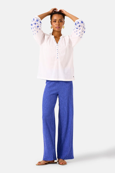 Pantalon bleu texturé de GARCIA, coupe ample avec une texture plissée et souple, porté avec un chemisier blanc brodé.
