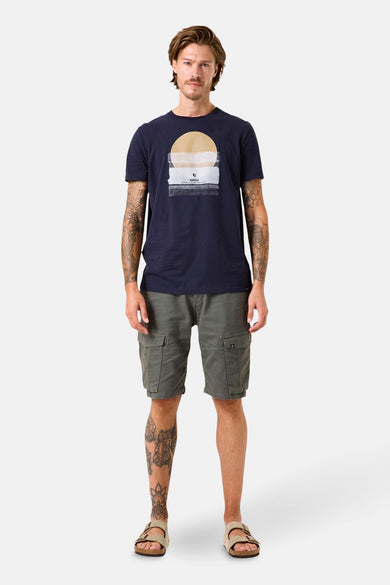 T-shirt bleu à manches courtes de GARCIA, avec un motif graphique sur le devant, porté avec un short cargo kaki et des sandales.
