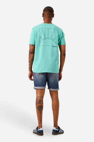 T-shirt à manches courtes vert de GARCIA, imprimé soleil au dos, porté avec un short en jean délavé et des baskets bleues.
